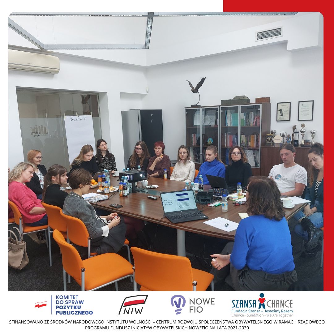 Grupa osób siedzi w sali konferencyjnej i słucha prezentacji kobiety.